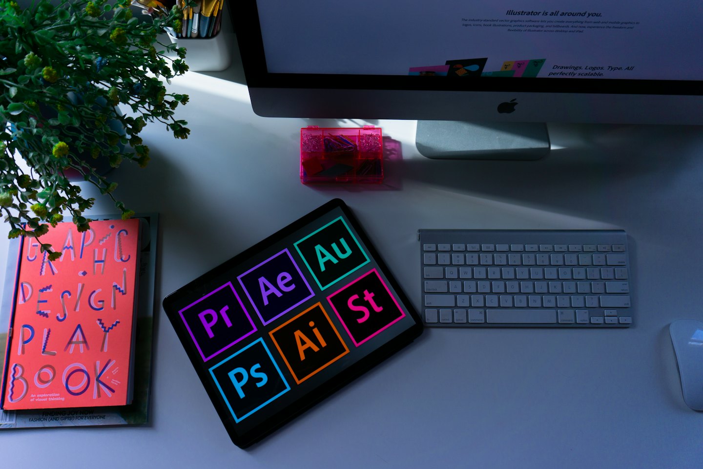 Graphic designer's organized desk with computer, tablet, and design tools.
