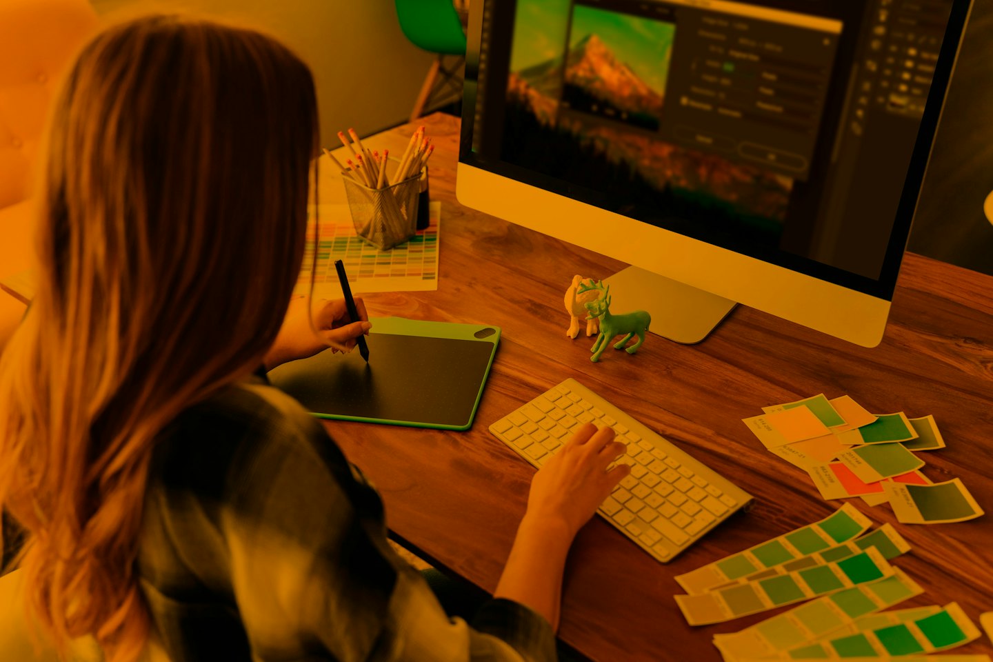 Graphic designer edits image on computer with tablet and keyboard.